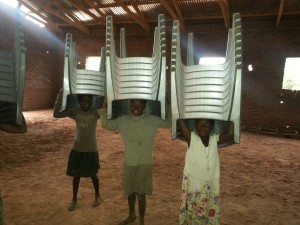 Girls in Malawi carry chairs 